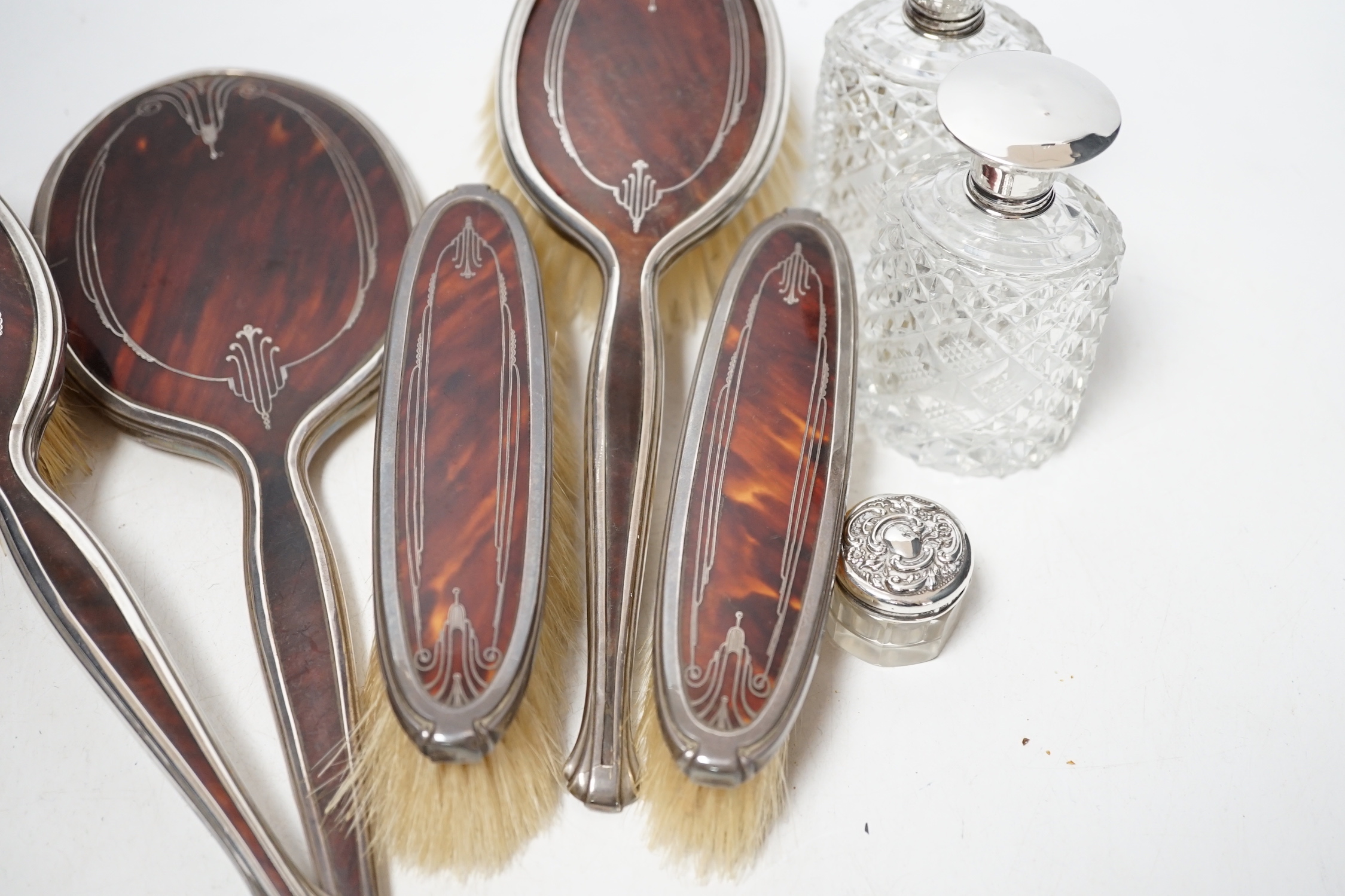 A George V silver and tortoiseshell pique mounted dressing table set, Adie Bros, Birmingham, 1934, and three silver topped toilet jars.